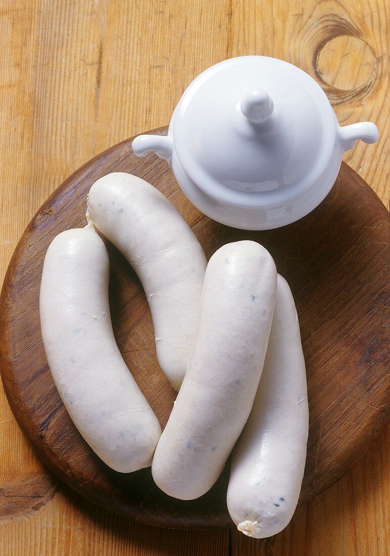 Four Weisswurst (white sausages) & mustard pot on wooden board