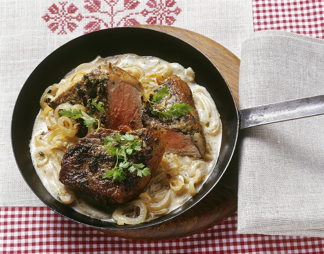 Steak in onion and white wine sauce in a frying pan