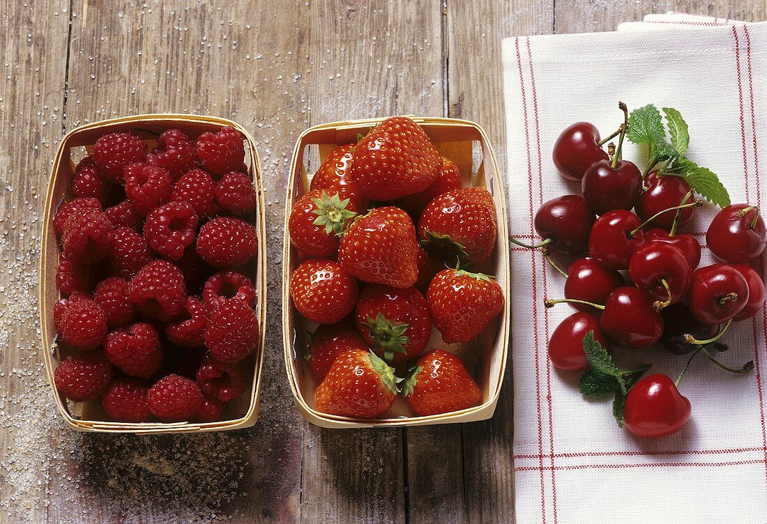 Himbeeren, Erdbeeren in Holzschachtel,Kirschen auf Küchentuch