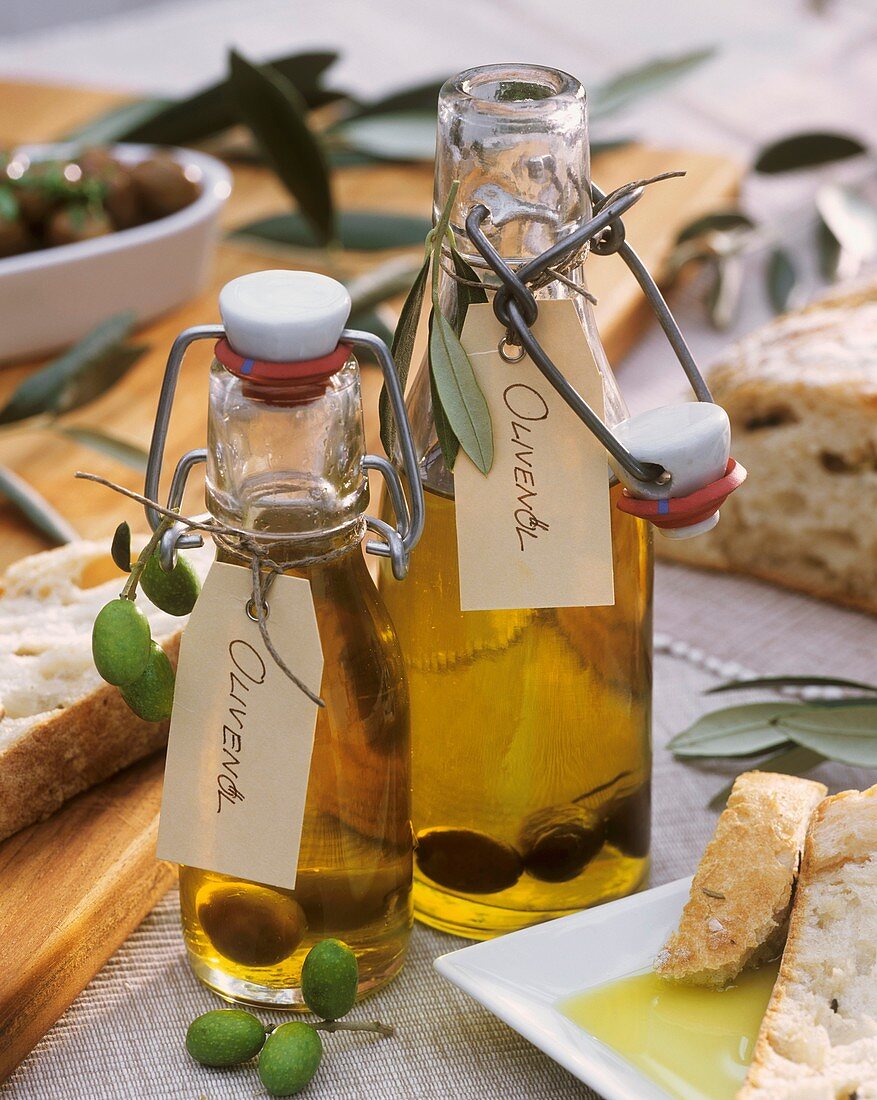 Zwei Glasflaschen mit Olivenöl, eingelegte Oliven, Ciabatta