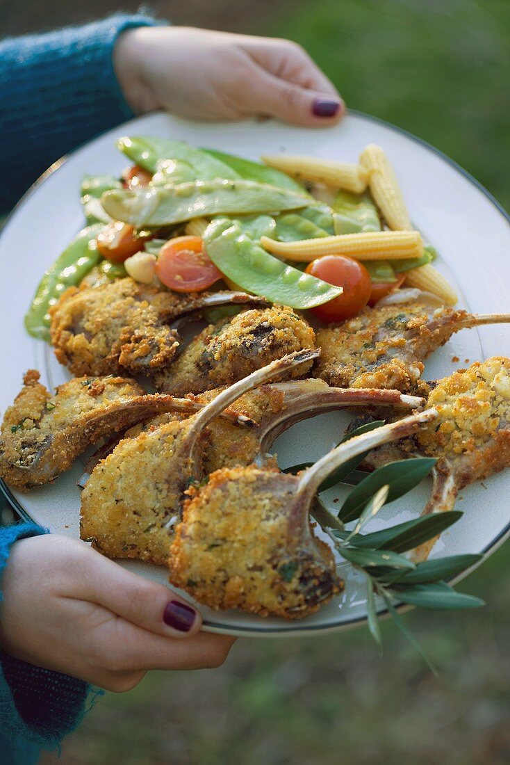 Woman holding a platter of breaded lamb chops & vegetables