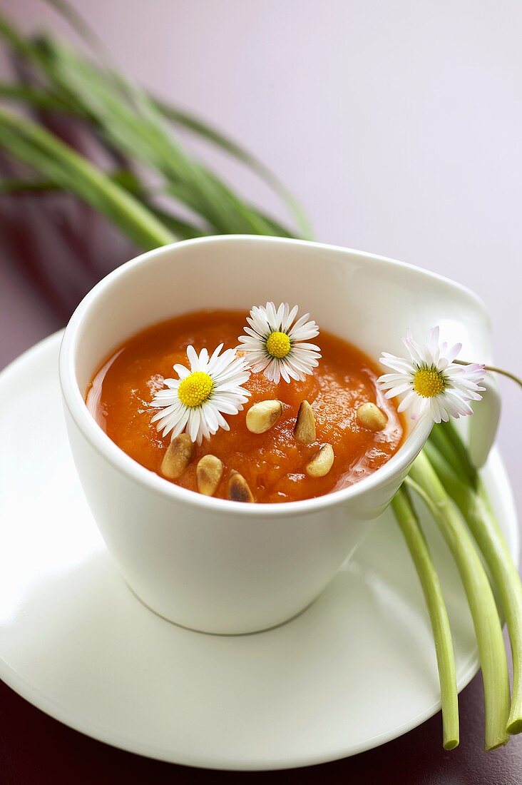 Karottensuppe mit Pinienkernen und Gänseblümchen in Tasse