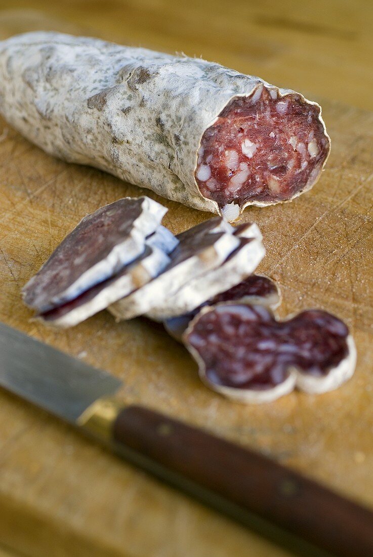 Partly-sliced salami on a wooden board with a knife
