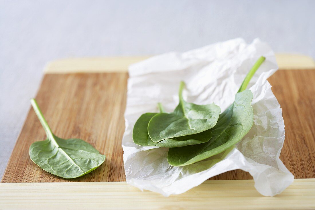 Fresh spinach leaves on paper and a wooden board