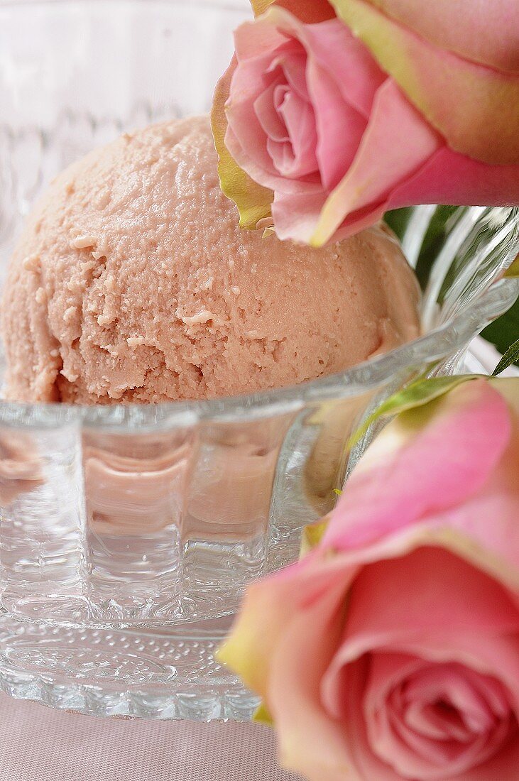A scoop of rose ice cream in a glass dish with pink roses