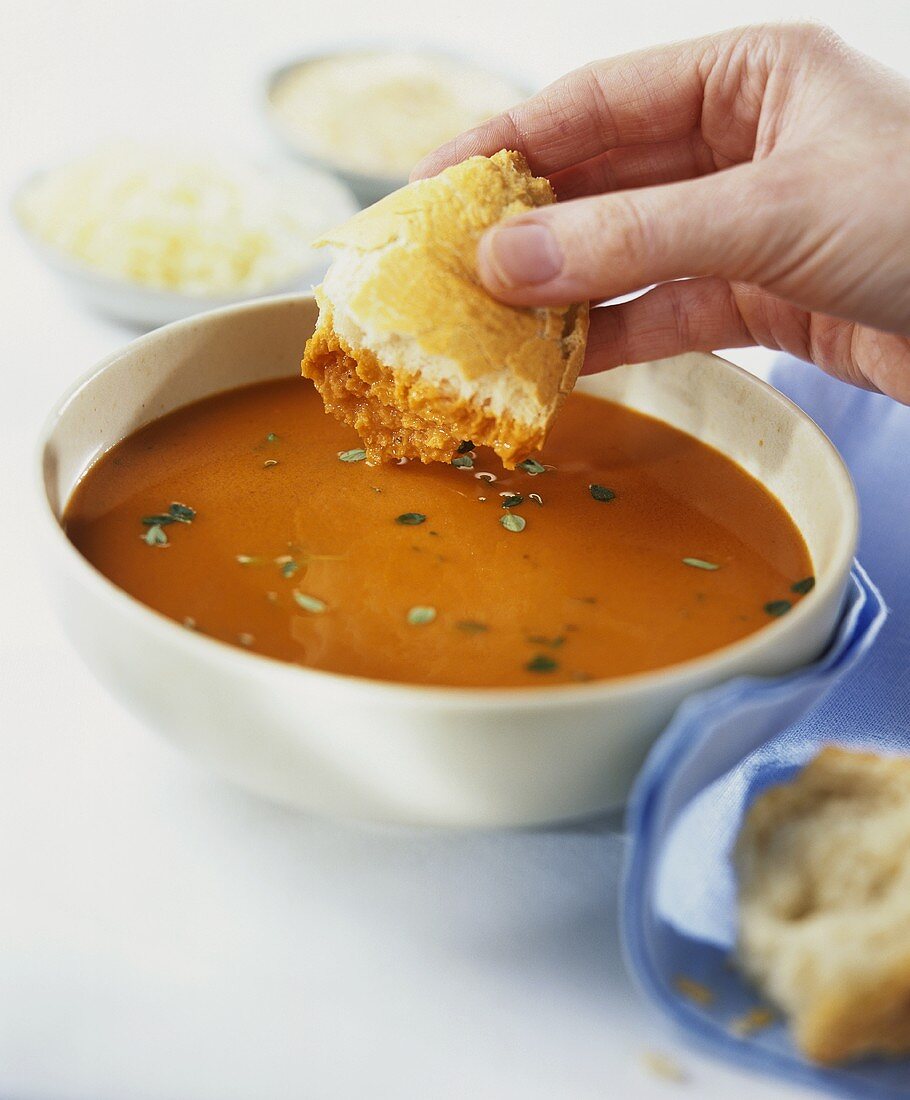 Man dipping white bread into a bowl of tomato soup