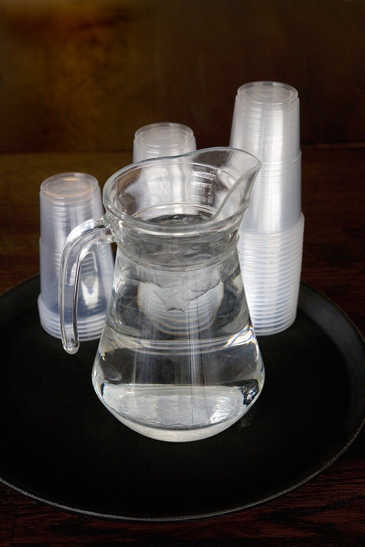 Karaffe mit Wasser und Plastikbechern auf einem Tablett