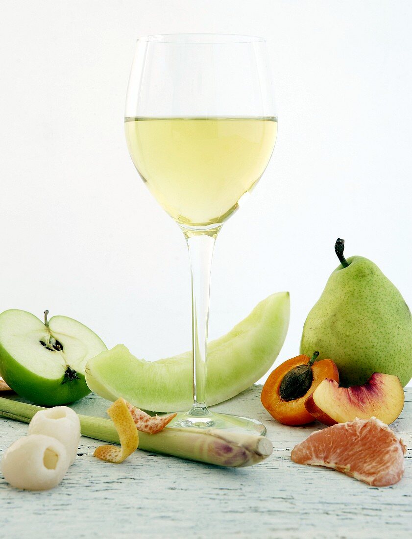 Glass of white wine surrounded by various fruits (aromas)