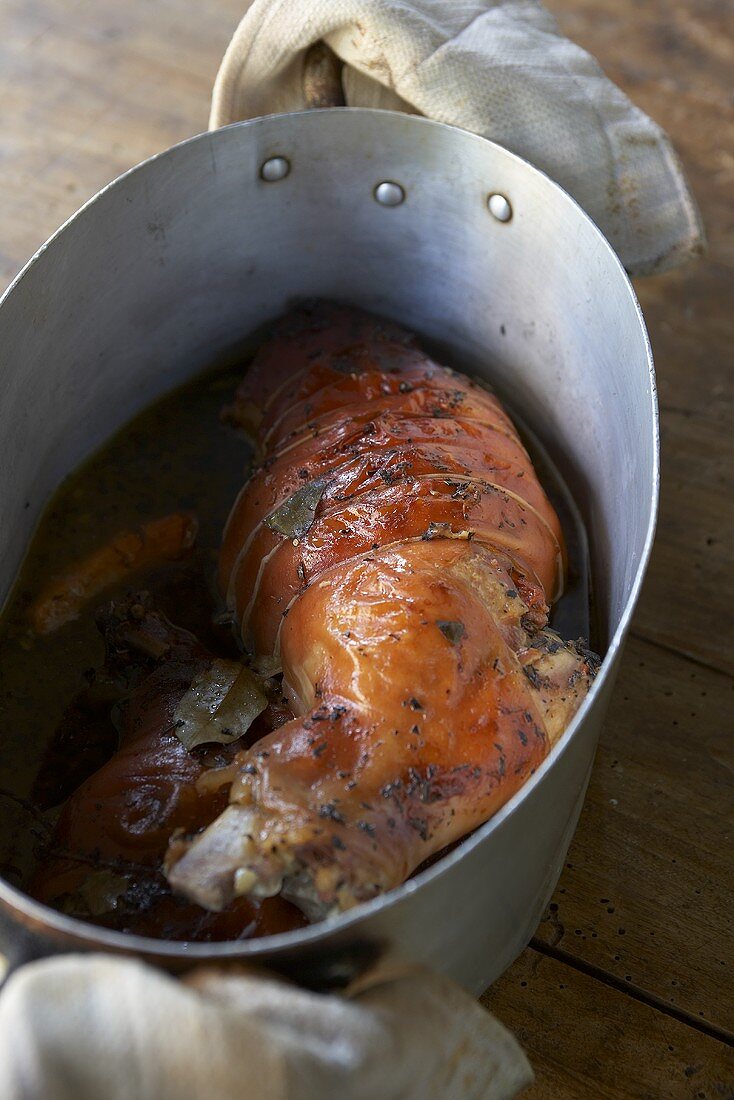 Leg of suckling pig in beer sauce in a roasting tin