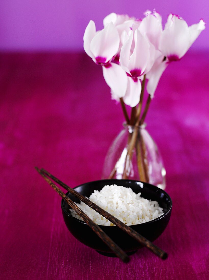 A bowl of rice with chopsticks, vase of flowers