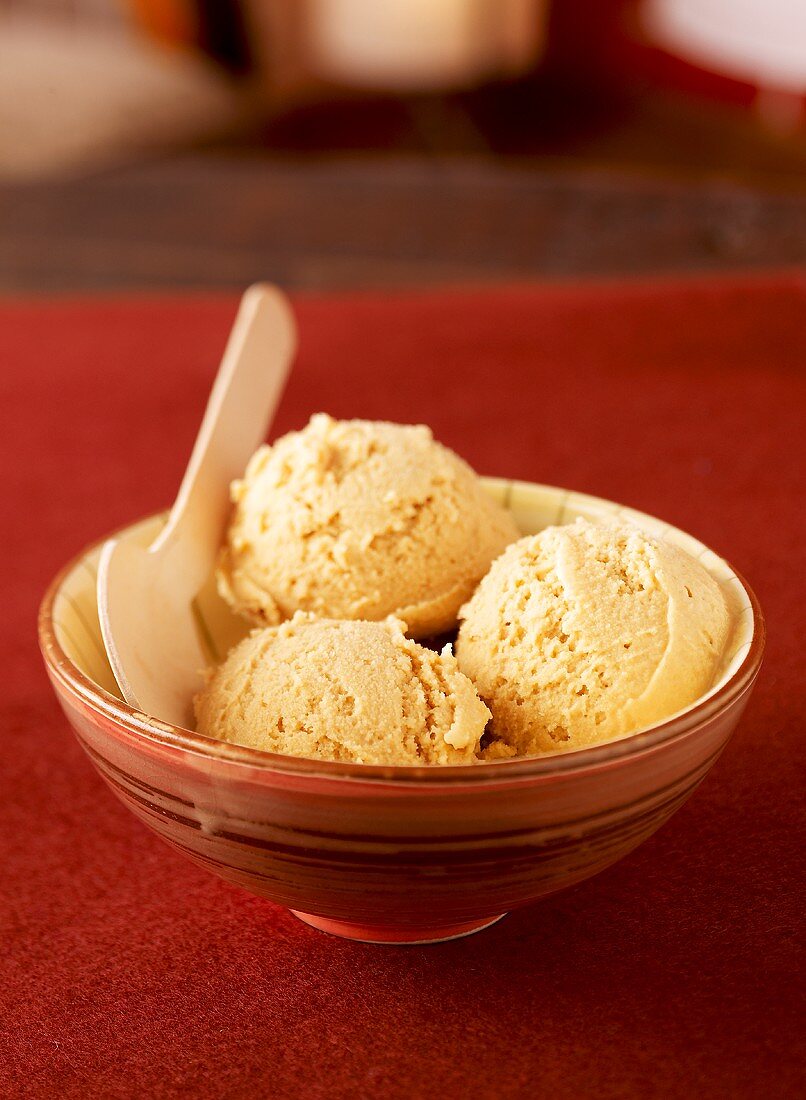 Three scoops of caramel ice cream in bowl with wooden spoon