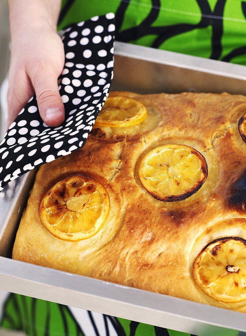 Frau hält Blech mit Zitronen-Focaccia in den Händen