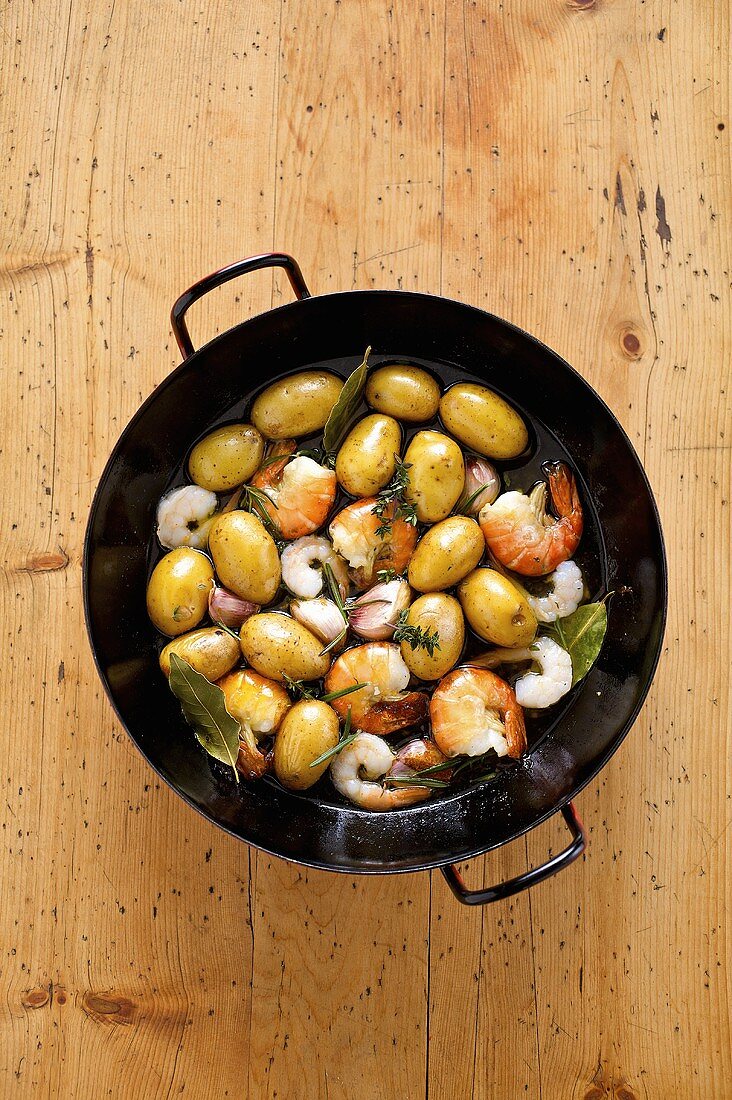 Fried prawns and potatoes with herbs in a frying pan