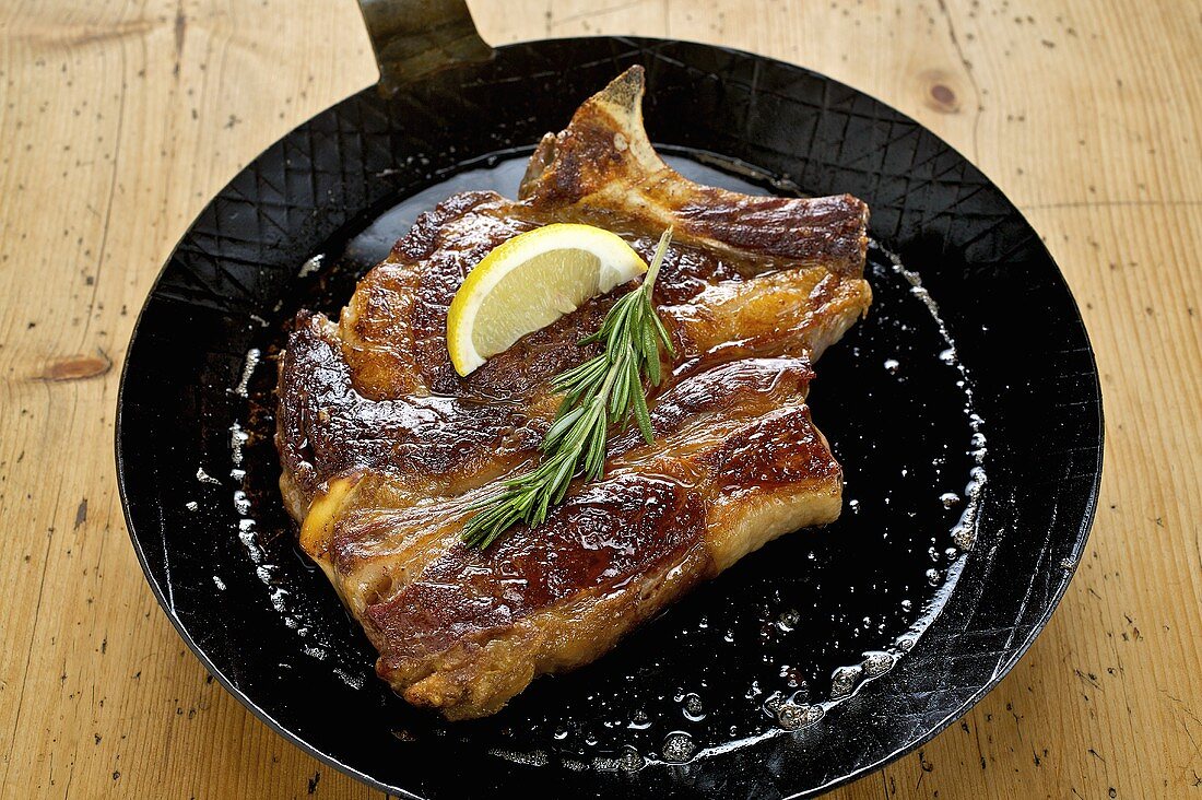 Fried prime rib of pork in a frying pan with rosemary