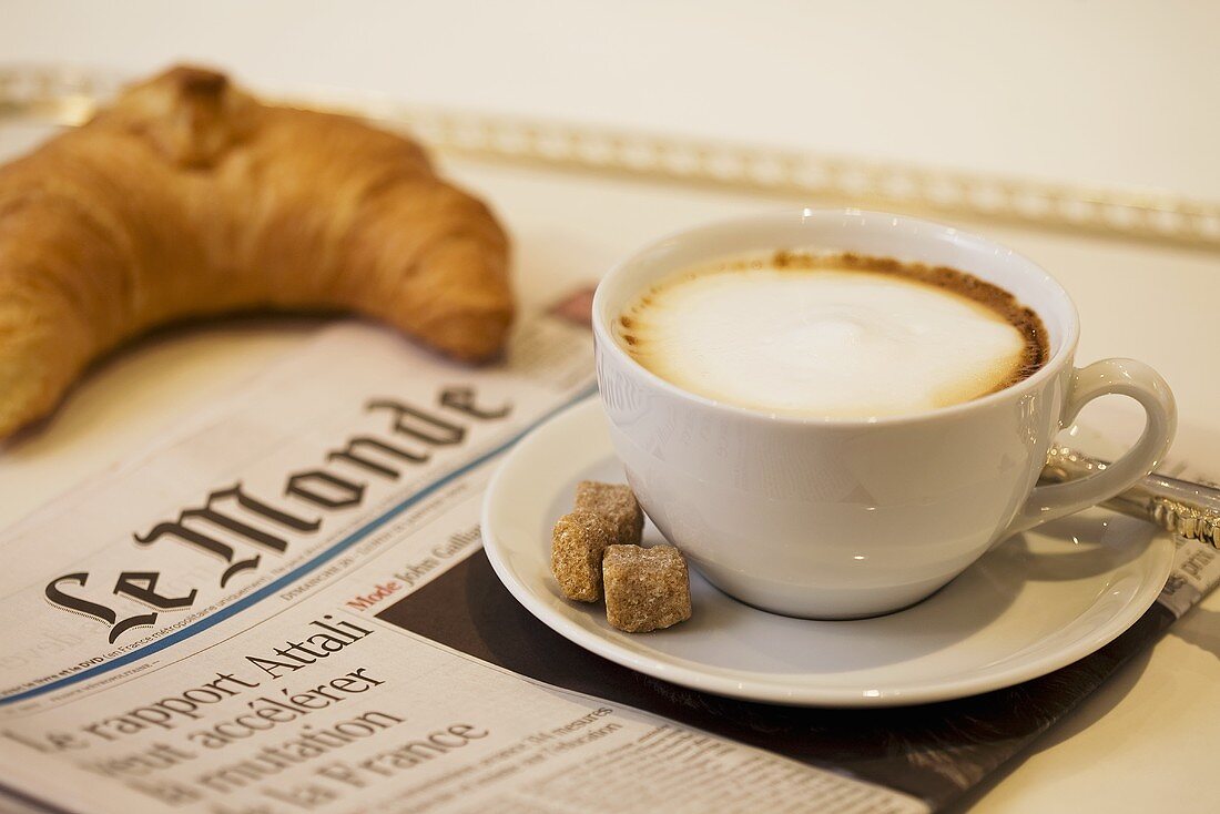 Milchkaffe auf französischer Zeitung mit einem Croissant