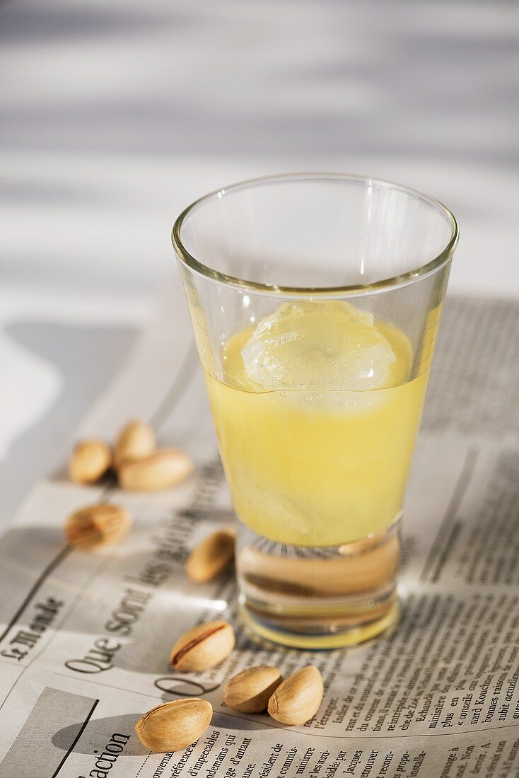 A glass of pastis with ice on a newspaper with pistachios
