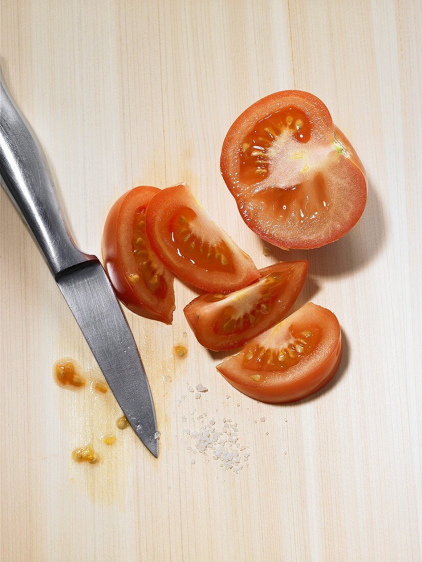 Tomato, partly cut into wedges, with salt and a knife
