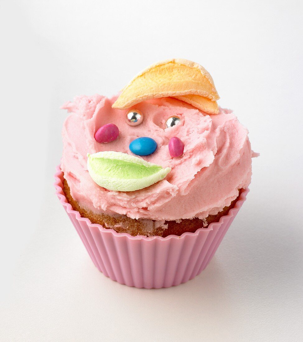 Cupcake with buttercream and amusing face made from sweets