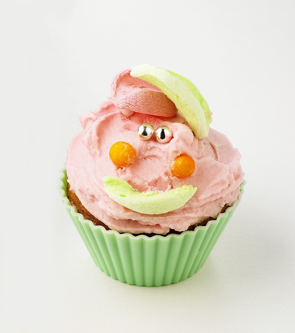 Cupcake with buttercream and amusing face made from sweets