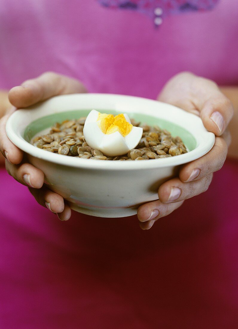 Hands holding a dish of lentils with boiled egg