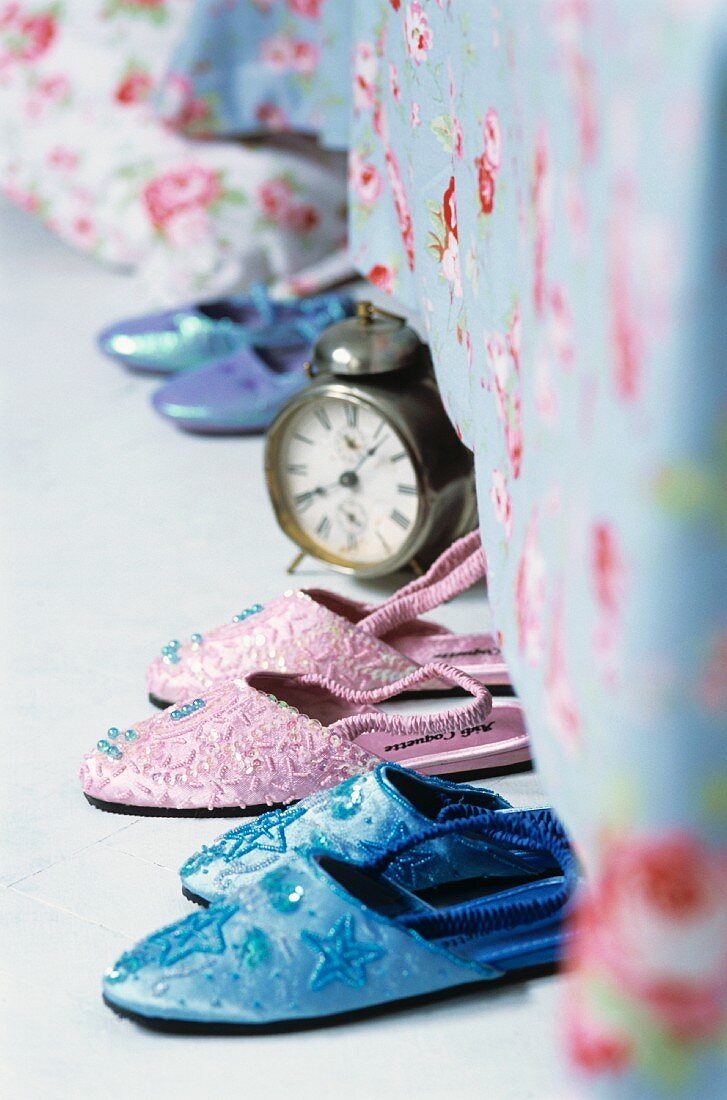 Indoor shoes and an alarm clock by a bed