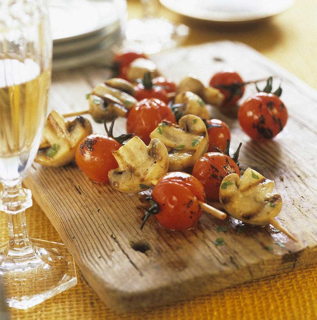 Grilled tomato and mushroom kebabs on a wooden board