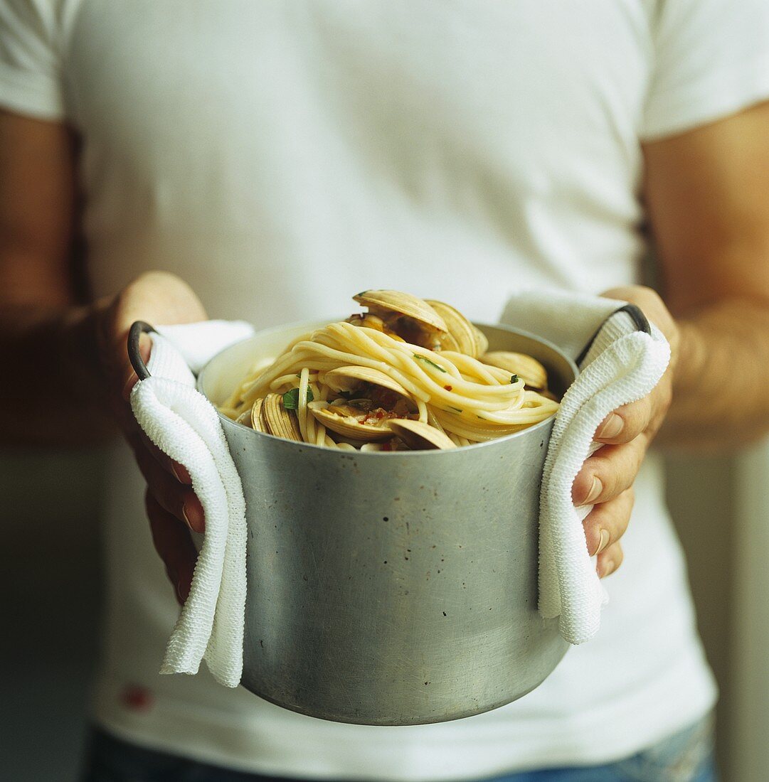 Mann hält einen Topf mit Spaghetti Vongole