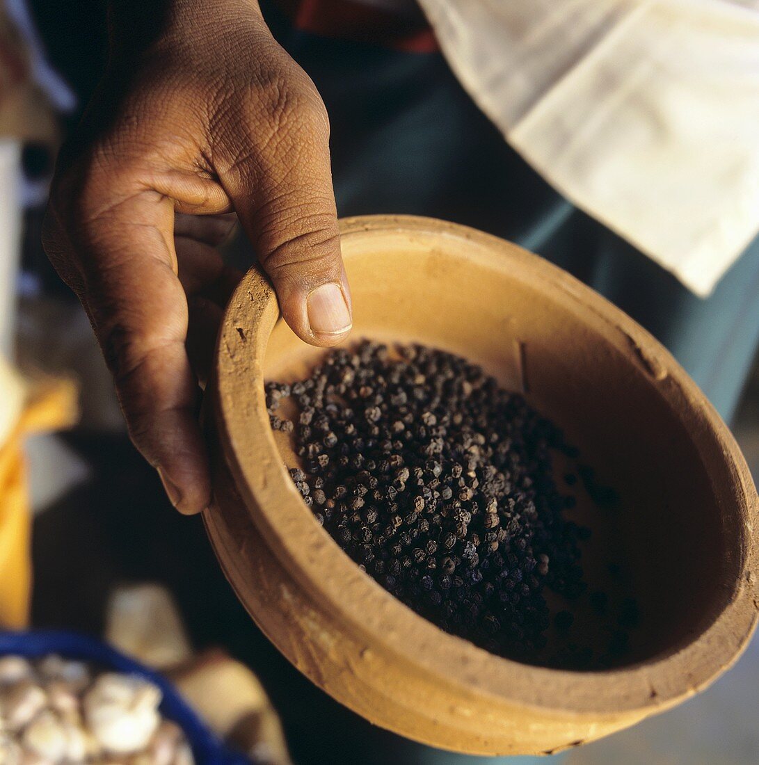 Man holding terracotta bowl of black peppercorns