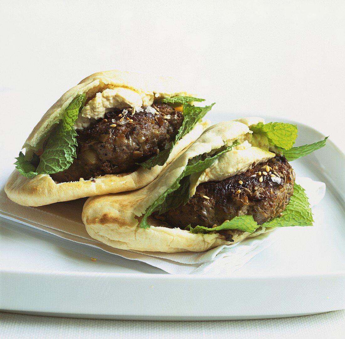 Two pita breads filled with lamb burgers, hummus and mint