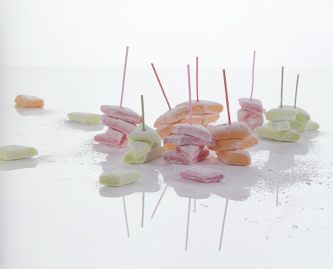 Different coloured marshmallows on sticks with icing sugar