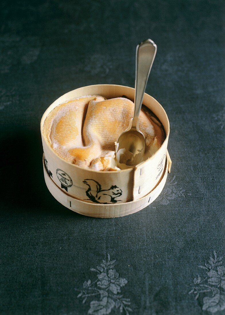 Soft cheese in a wooden box with a spoon