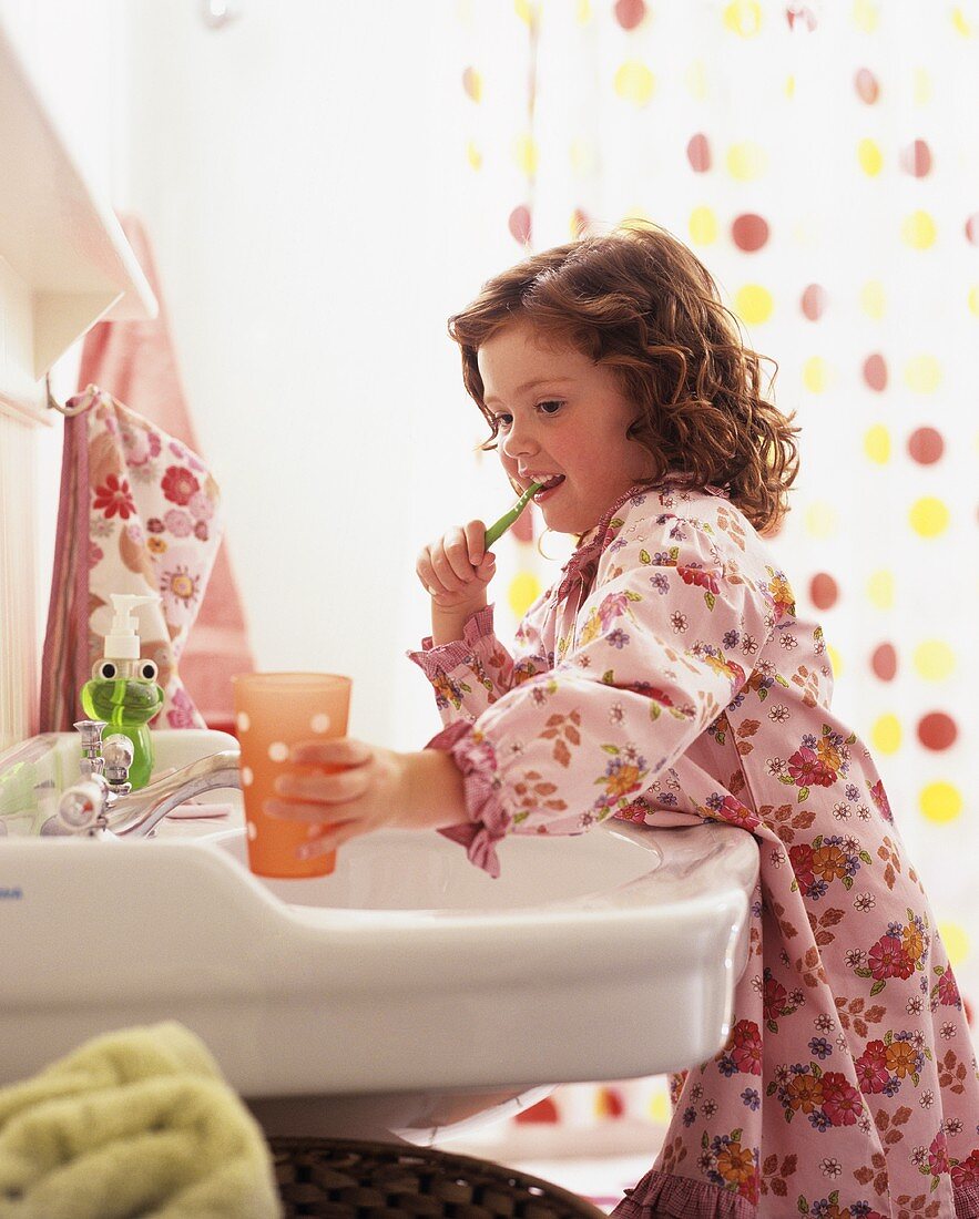 Little girl in bathrobe brushing her teeth