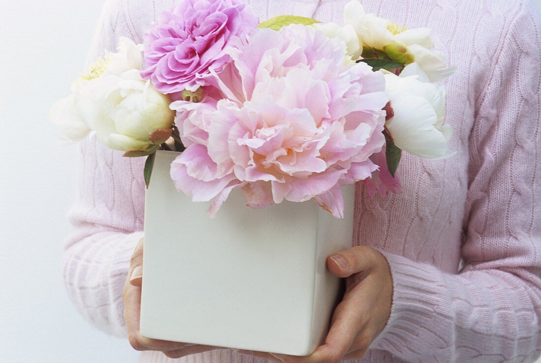 Woman holding vase of roses and white peonies