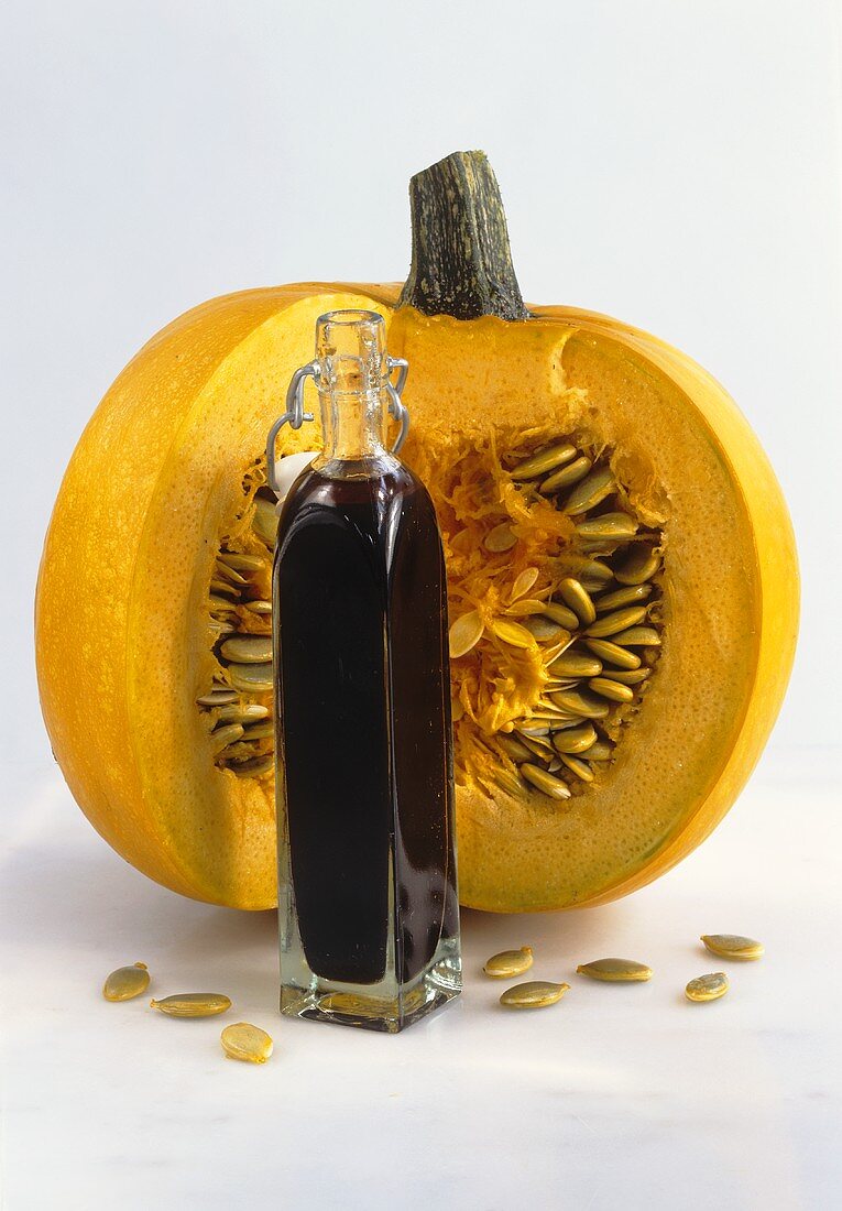 Bottle of pumpkin seed oil in front of pumpkin with section removed