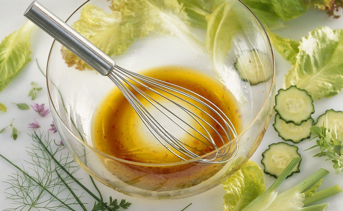 Red wine vinegar and olive oil dressing in glass bowl, salad ingredients