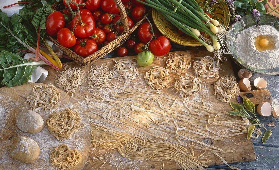 Home-made pasta and pasta dough on wooden board, vegetables