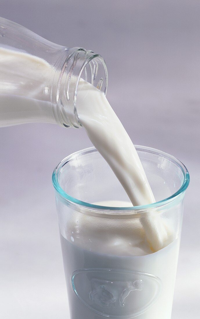 Aus einer Milchflasche Milch in ein Glas gießen