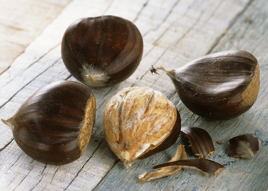 Three unshelled and one shelled sweet chestnut on wooden background