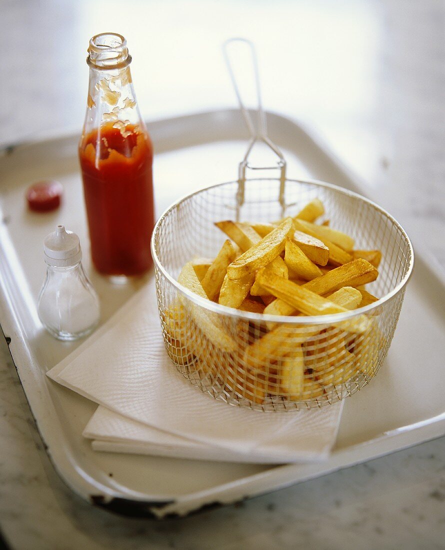 Pommes frites im Frittierkorb mit Ketchup und Salz