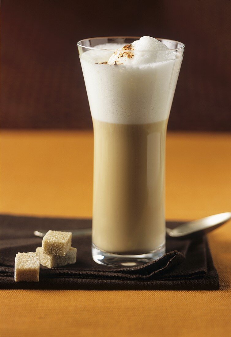 Glass of milky coffee with brown sugar cubes