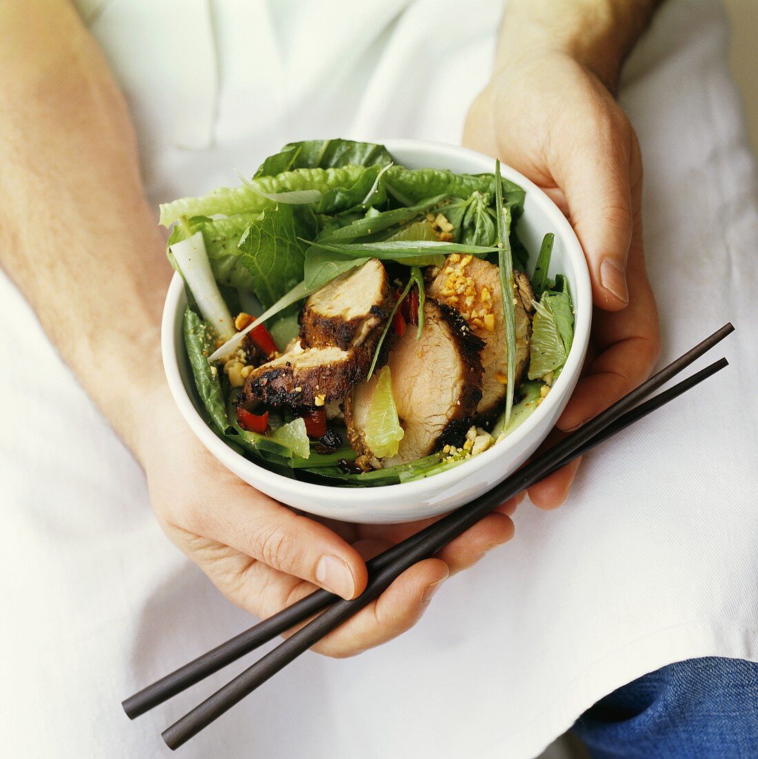 Man holding bowl of pork, salad leaves and peanuts