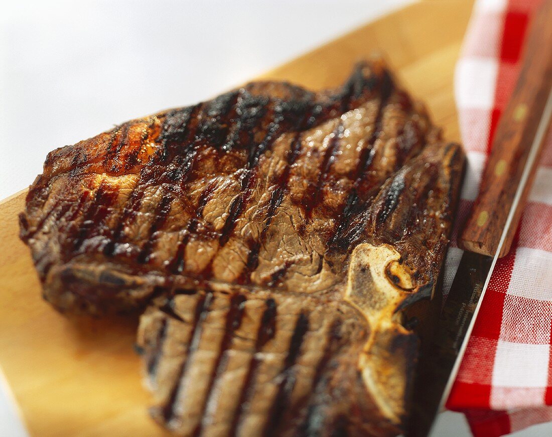A grilled T-bone steak on a wooden board with a knife