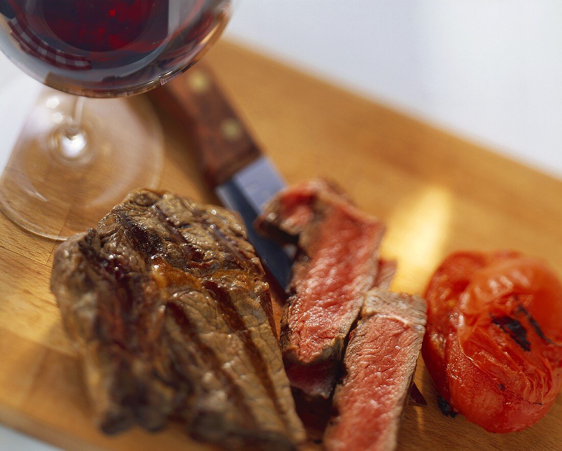 A grilled ribeye steak with tomatoes and red wine