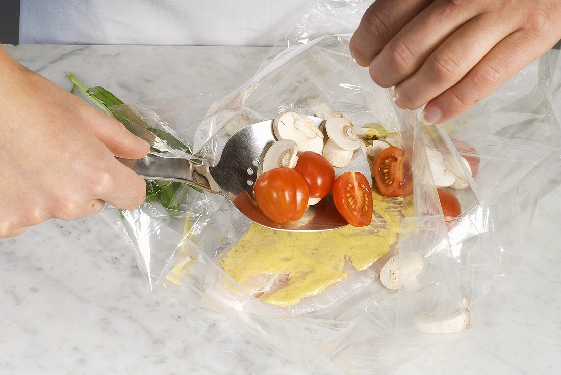 Putting tomatoes and mushrooms into a roasting bag