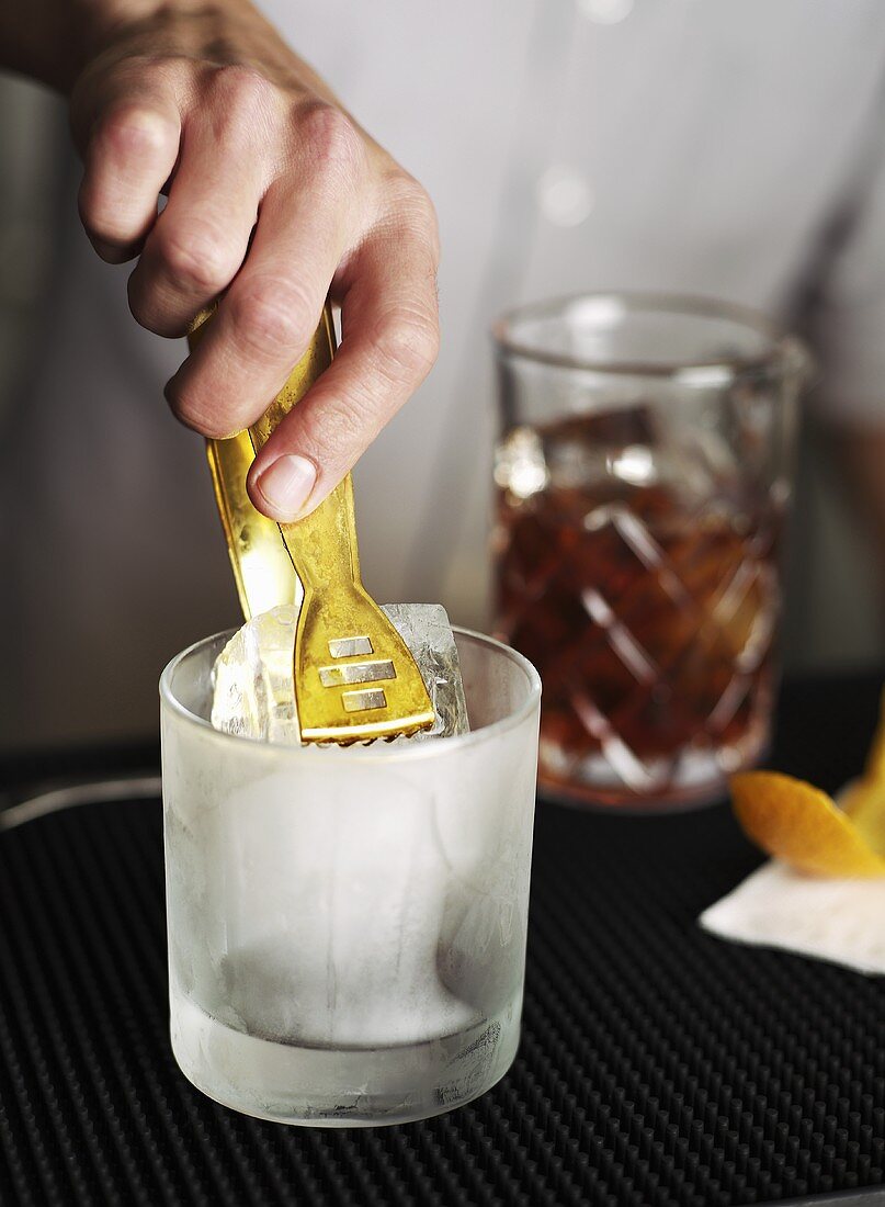 A bartender placing ice cubes in a glass