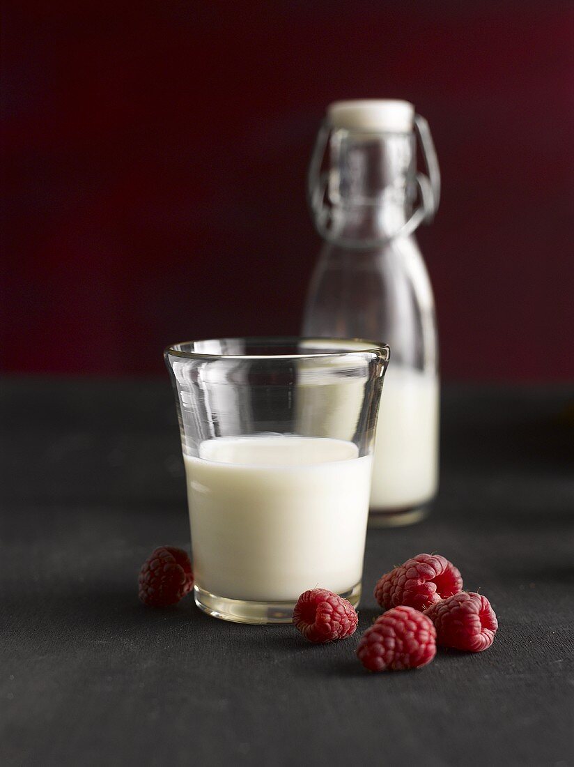 A glass of milk, raspberries and a bottle of milk
