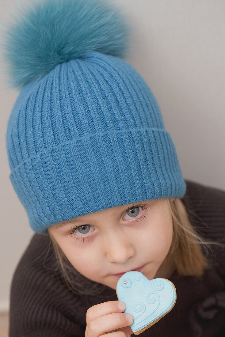 A little girl with a woolly hat eating a heart-shaped biscuit