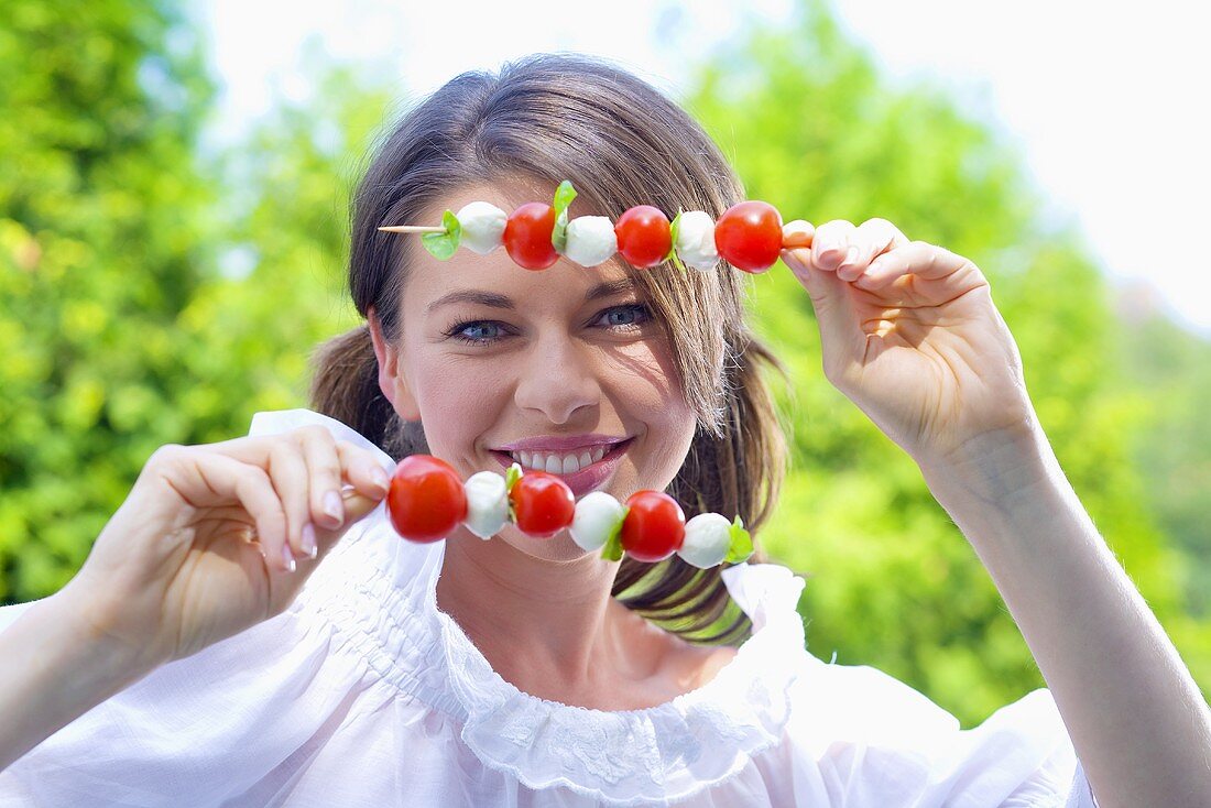 Junge Frau mit Tomaten-Mozzarella-Spiesschen