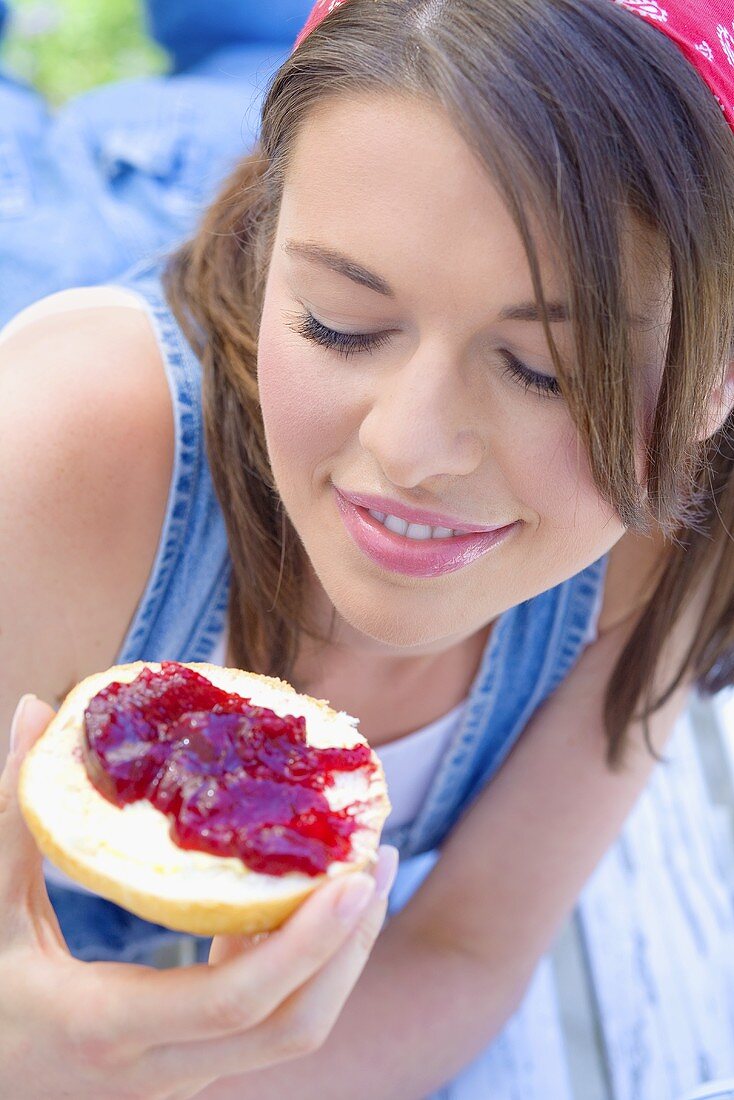 Young woman eating bread roll with jam