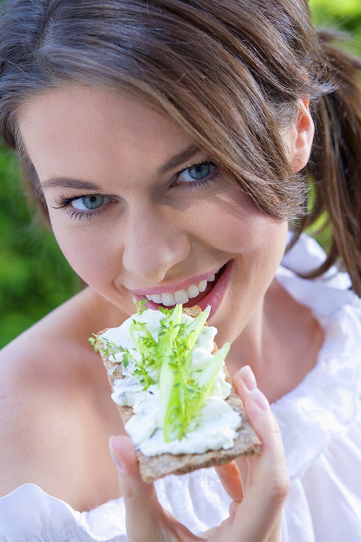 Junge Frau isst Knäckebrot mit Hüttenkäse und Gurke
